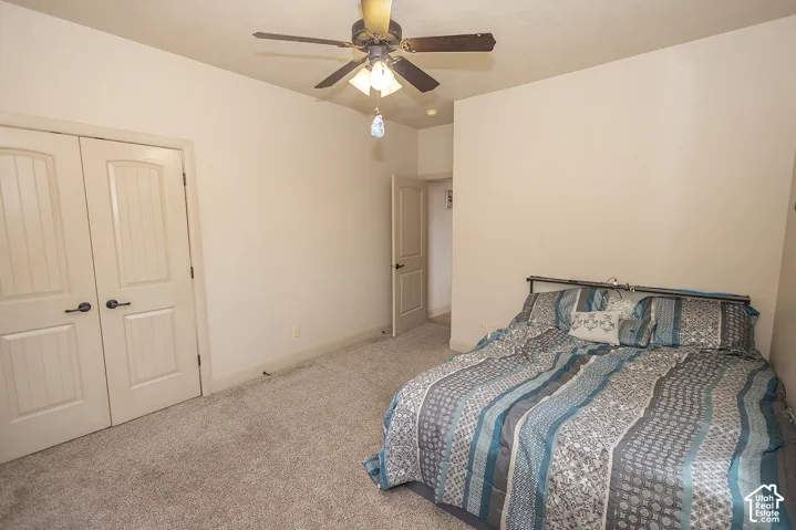 Carpeted room featuring a ceiling fan with integrated lighting, a metal bed frame, and two panel doors with dark hardware