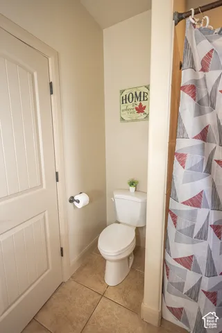 Ceramic tile flooring, white toilet, and paneled interior door