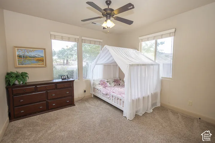 Neutral tone wall finish, multiple windows, ceiling fan with integrated lighting, and carpeted flooring