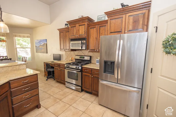 Kitchen featuring wood cabinetry, stainless steel appliances, tile flooring, and light-toned countertops