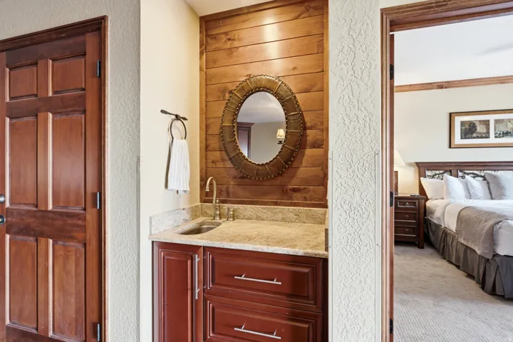 Wood plank accent wall with an oval mirror, a stone-finish countertop, and a built-in wood-finish vanity with storage