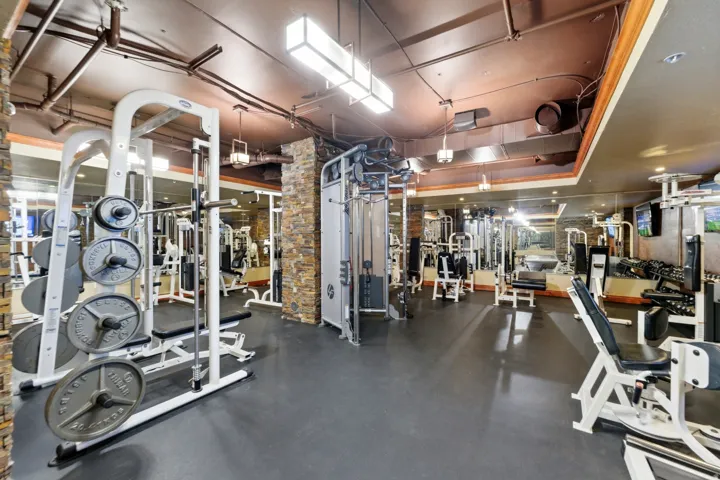Fitness center featuring extensive exercise equipment, mirrored walls, exposed ductwork, recessed lighting, and stone veneer columns