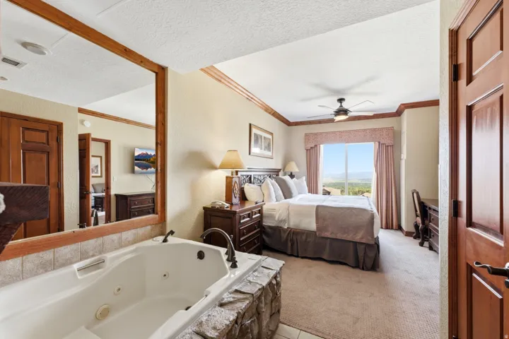 Soaking tub with stone surround, wood-finish trim, ceiling fan, and carpeted flooring