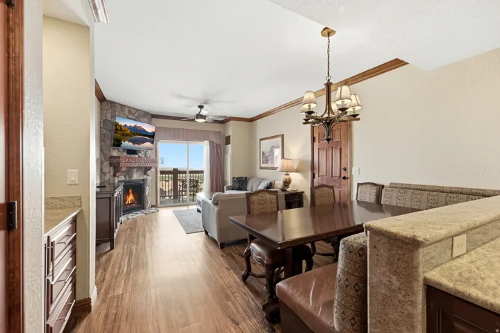 Wood-finish flooring throughout, a stone-clad corner fireplace with a carved mantel, a ceiling fan, a private balcony, and a built-in dining nook with upholstered seating