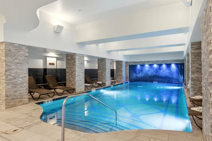 Indoor swimming pool with tile surround, stone-clad columns, and a back wall featuring water elements
