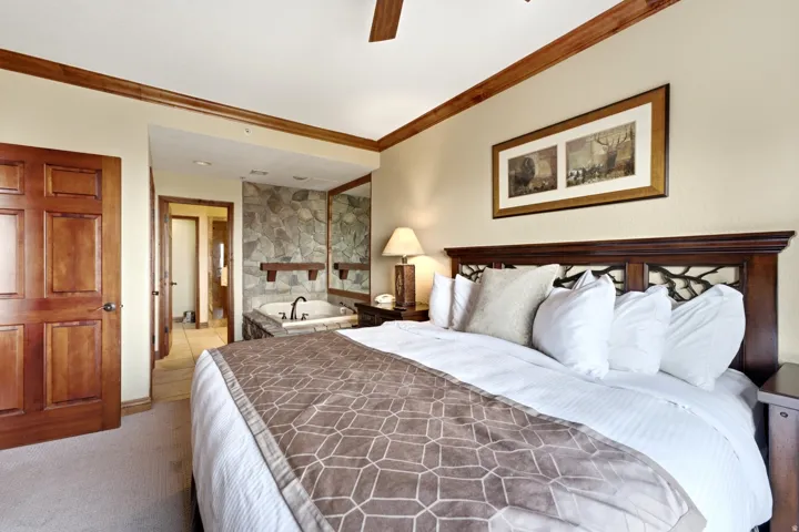 Built-in jetted tub with stone surround, wood-paneled doors, wood trim, and a ceiling fan