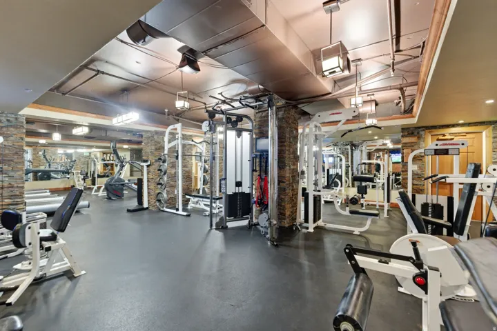 Fitness area featuring exposed ductwork, recessed lighting, and stone column accents