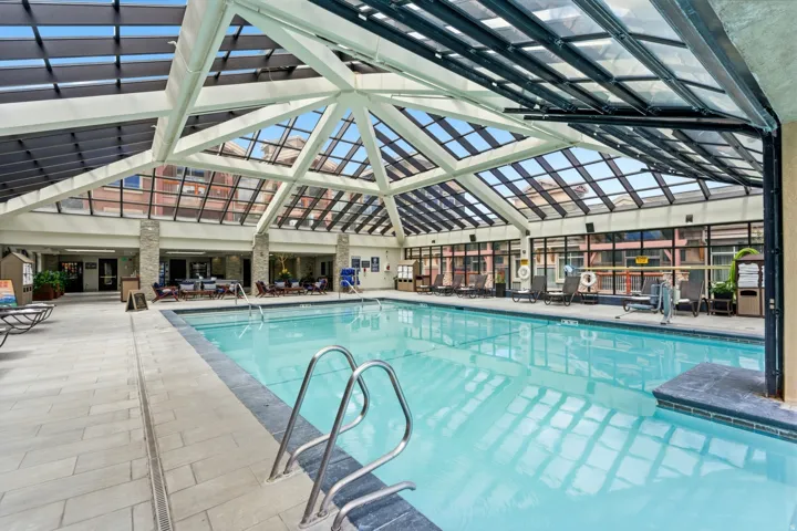 Indoor swimming pool with a glass-paneled ceiling, integrated ladder, and surrounding tiled deck