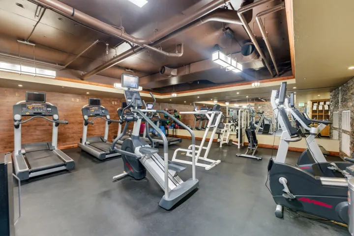 Fitness center featuring multiple cardio machines, exposed overhead ducts, a mirrored wall, and textured wall finishes
