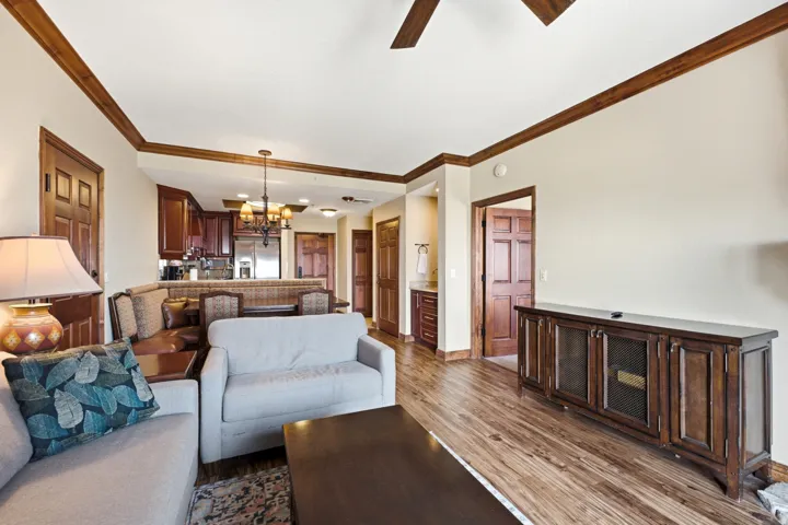 Open-concept living area featuring wood-finish flooring, a kitchen with dark wood cabinetry, a ceiling fan, and a built-in media console