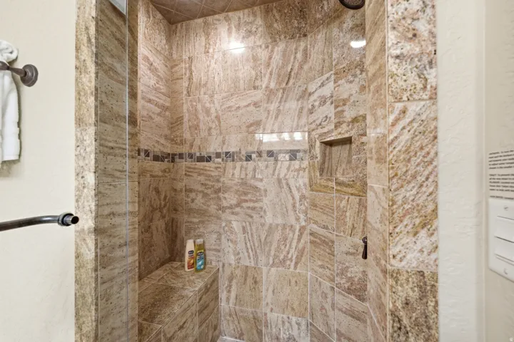 Tiled shower enclosure featuring a recessed niche, an integrated shower bench, a fixed shower head, and a decorative accent tile band