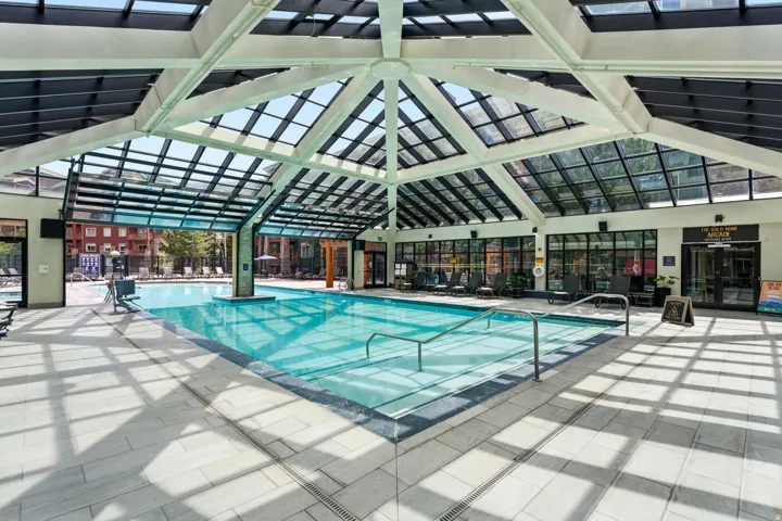 Indoor pool with a retractable glass roof system, light-toned tile decking, and stainless steel handrails