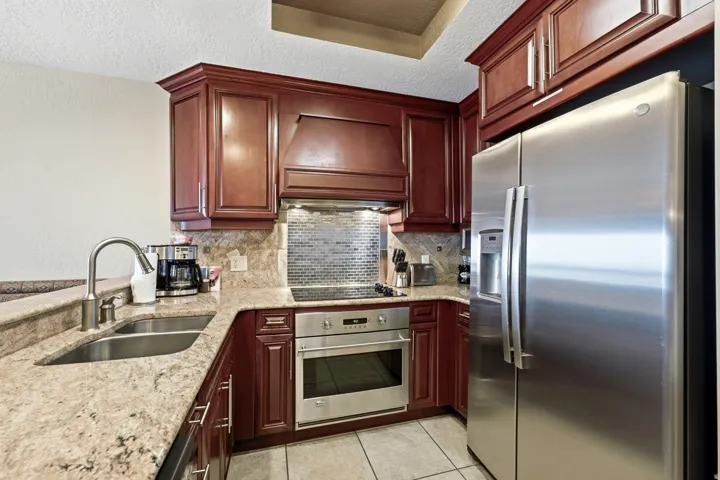 Kitchen featuring rich wood cabinetry, stainless steel appliances, granite countertops, a built-in oven, and a tile backsplash