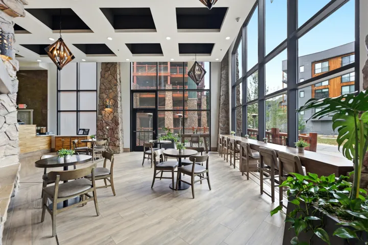 Expansive window wall, stone column accents, coffered ceiling, wood-finish flooring, and built-in wood bar seating