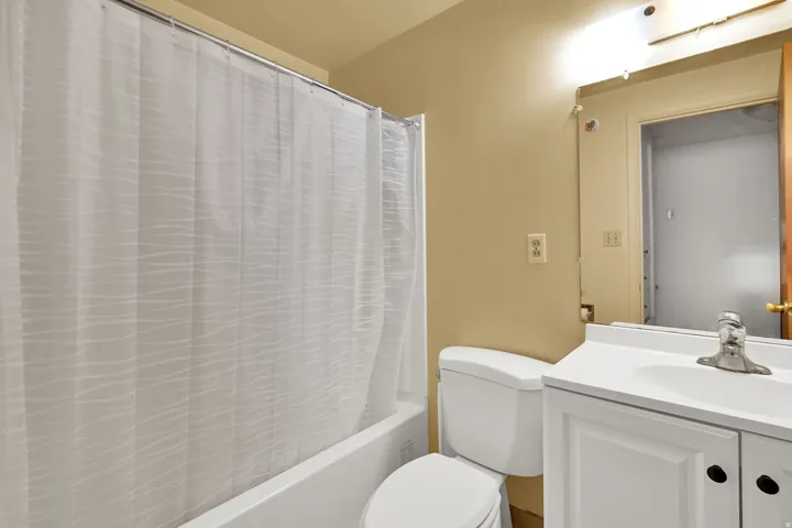 White tub and shower combination with a bright white vanity featuring an integrated sink, a chrome faucet, and a wall-mounted mirror with overhead lighting