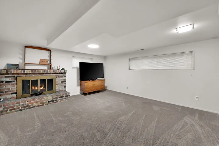 Brick fireplace with brass-finish doors, gray wall-to-wall carpeting, and a rectangular window with blinds