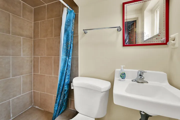 Tiled shower with a chrome shower rod, wall-mounted sink, toilet, and a framed mirror