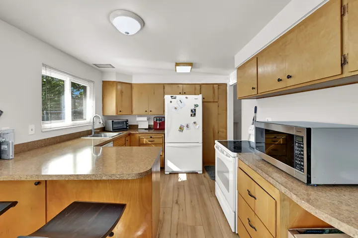 Kitchen featuring wood-finish flooring, light wood cabinetry, white appliances, and a stainless steel sink