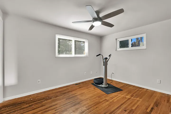 Hardwood flooring, light gray walls, white trim, ceiling fan with integrated lighting, and multiple windows
