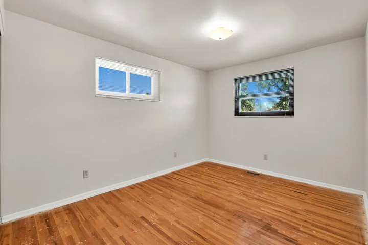 Wood-finish flooring with white baseboards, two windows with blinds, and an overhead light fixture