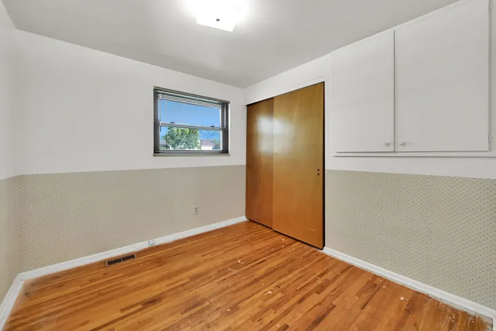 Wood-finish flooring, built-in overhead cabinetry, and a window with a metal frame