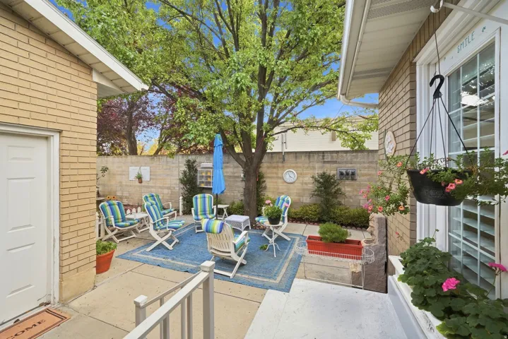 Paved patio area with a privacy wall, mature trees, and an exterior brick finish