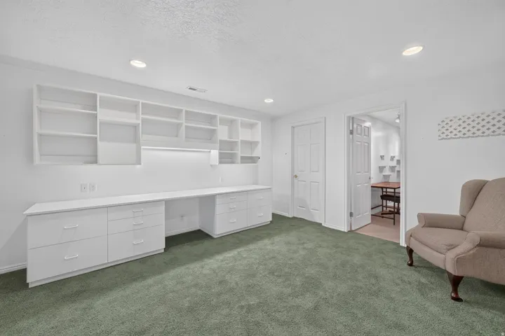 Built-in shelving, integrated desk, white cabinetry, recessed lighting, and green carpeting
