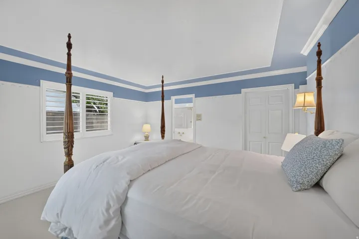 Recessed ceiling detail with crown molding, window with plantation shutters, paneled door, and carpeted flooring