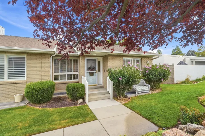 Brick exterior with white trim, concrete walkway, and established landscaping featuring mature shrubs
