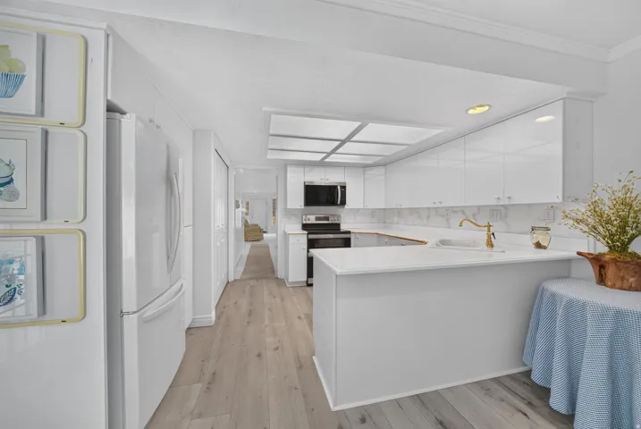 Bright kitchen with recessed lighting, white cabinetry, integrated appliances, wood-finish flooring, and a white countertop with a gold-toned faucet