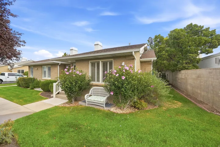 Brick exterior with white trim, established landscaping, concrete sidewalk, and a block wall along the property line