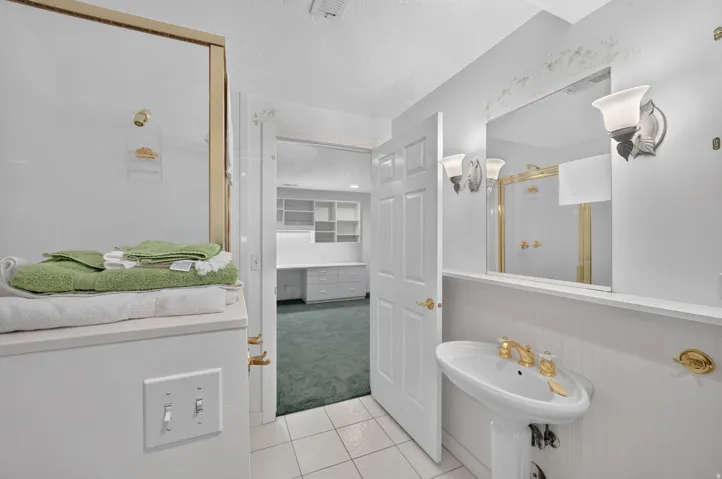 Pedestal sink with gold-finish faucet, wall-mounted mirror, vanity lighting, and tiled flooring