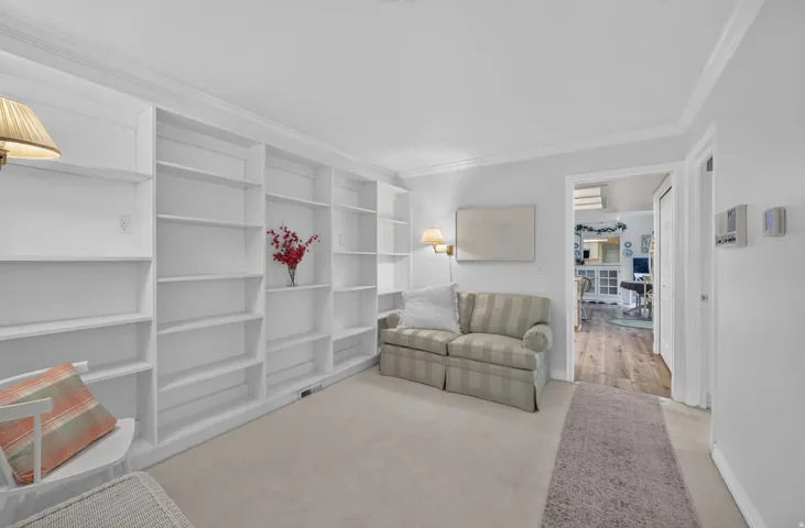 Built-in shelving with crown molding, wall-mounted sconces, and neutral carpeting