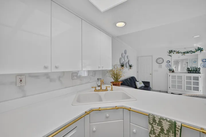 White glossy cabinetry with knob pulls, double basin sink with brass-finish faucet, white countertop, and white marble-patterned backsplash