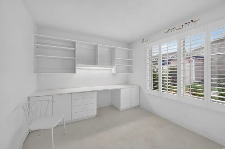 Built-in desk with integrated storage, overhead shelving, under-cabinet lighting, and white plantation shutters