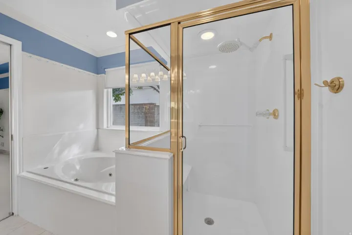 Built-in jetted tub, enclosed shower with gold-tone fixtures, recessed lighting, and a transom window