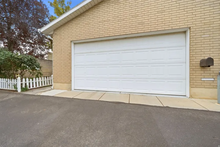 Brick exterior with a white panel garage door, concrete driveway, and white picket fence