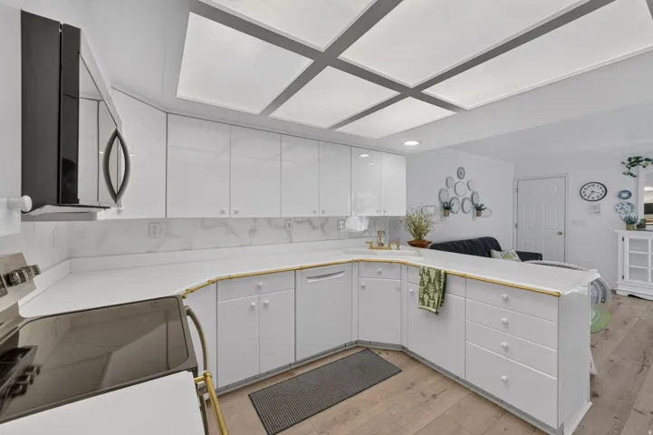 U-shaped kitchen featuring white cabinetry, light countertops, integrated sink, and wood-finish flooring