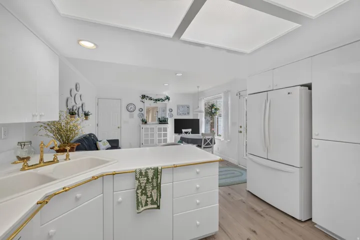 White cabinetry, white countertop, gold-finish faucet, recessed lighting, and wood-finish flooring
