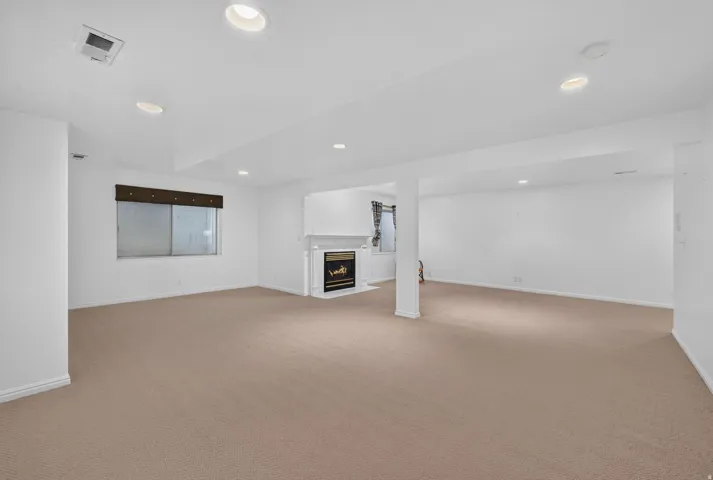Expansive carpeted area with recessed lighting, a built-in fireplace, and a window