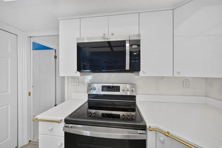 White cabinetry with integrated appliances, stainless steel range, and white countertops
