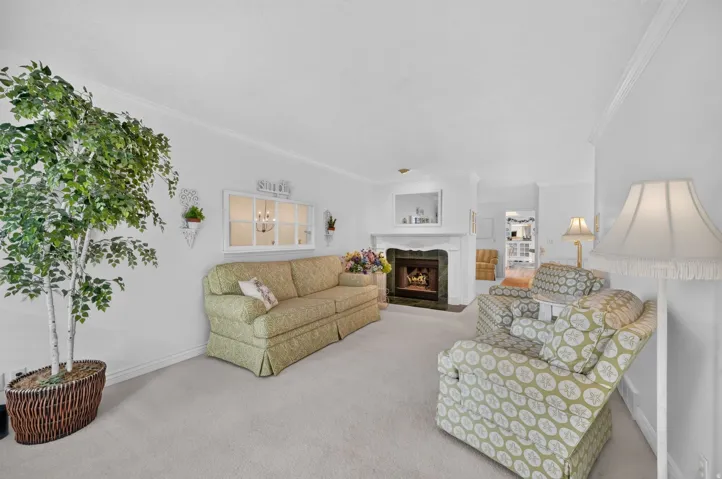 Living area featuring a fireplace with a stone surround, crown molding, and light-colored carpeting