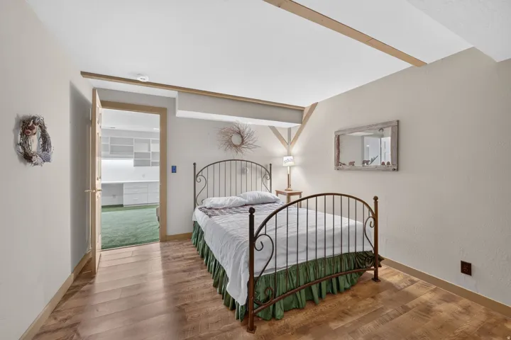 Wood-finish flooring with exposed ceiling beams and a doorway revealing built-in shelving