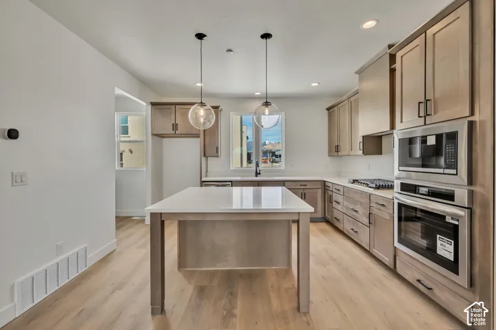 Spacious kitchen featuring light wood-finish cabinetry, stainless steel appliances, a center island with a light-toned countertop, and wood-finish flooring