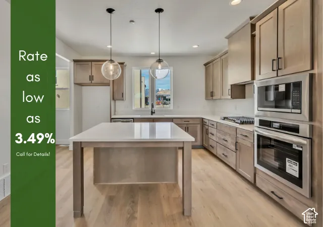 Kitchen featuring a central island, wood-finish flooring, light wood-toned cabinetry, stainless steel appliances, and pendant lighting