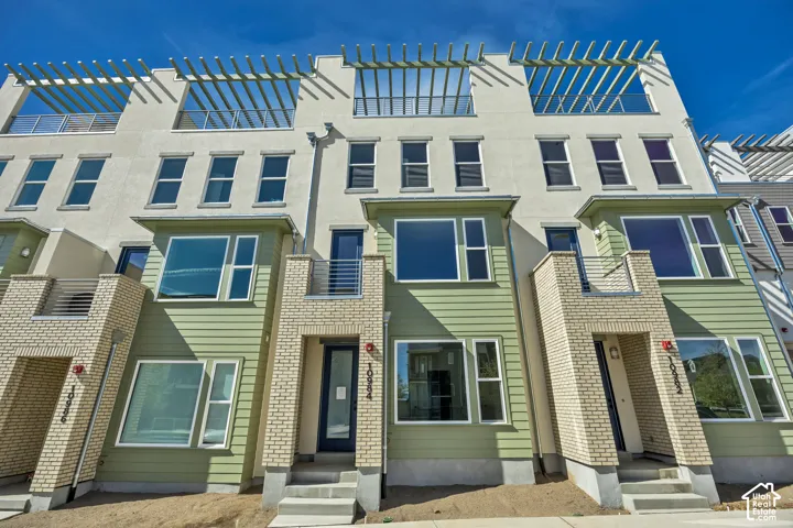 Modern townhouse exterior featuring light green siding, light brick accents, and multiple large windows