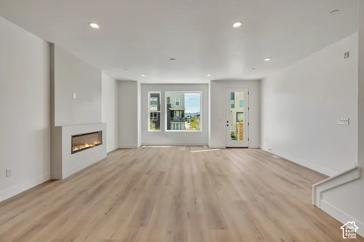 Spacious living area featuring wood-finish flooring, a modern linear fireplace, recessed lighting, and multiple windows