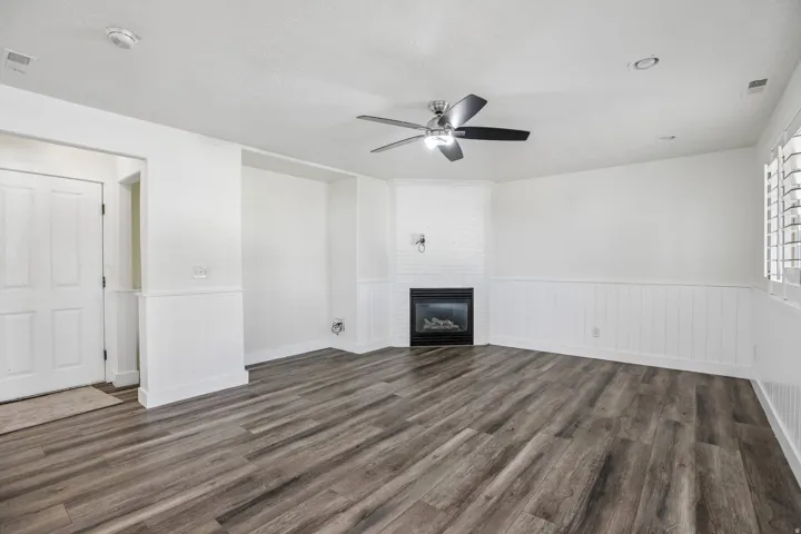 Wood-finish flooring, white paneled wainscoting, a built-in fireplace with a brick surround, and a ceiling fan