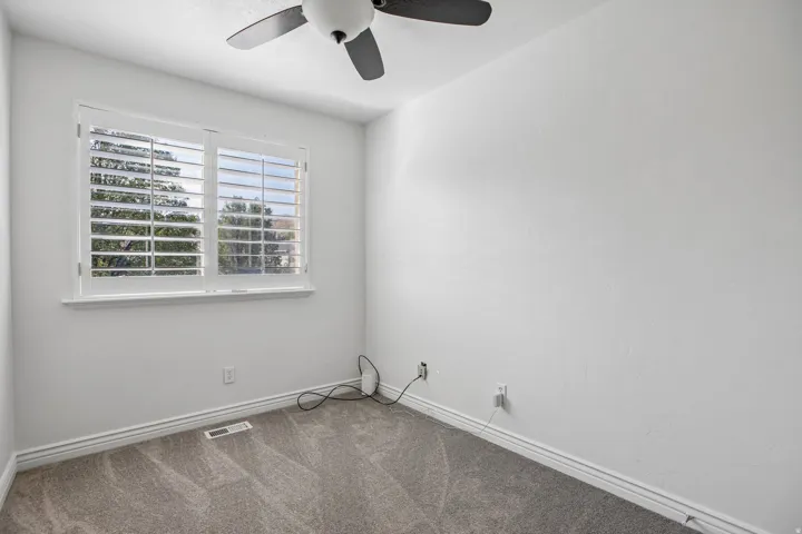 Window with plantation shutters, ceiling fan, white walls, and gray carpet