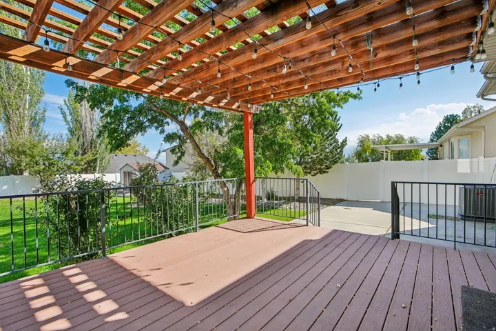Wood-finish deck with a slatted pergola, black metal railings, and a concrete patio